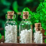 Homöopathische kügelchen in kleinen flaschen mit frischen blättern im hintergrund, homöopathiekonzept