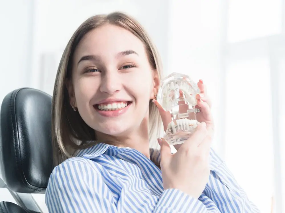 Portrait eines glücklichen attraktiven mädchens in einem zahnmedizinischen stuhl. lachendes mädchen beim zahnarzttermin mit einem kiefermodell in ihren händen