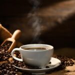 Tasse kaffee mit rauch und kaffeebohnen auf leinensack auf altem holz