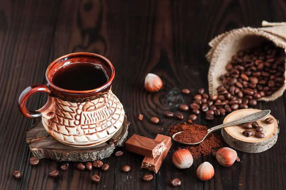 Heißer duftender kaffee in einer alten tontasse und kaffeebohnen mit nüssen auf dunklem holzhintergrund