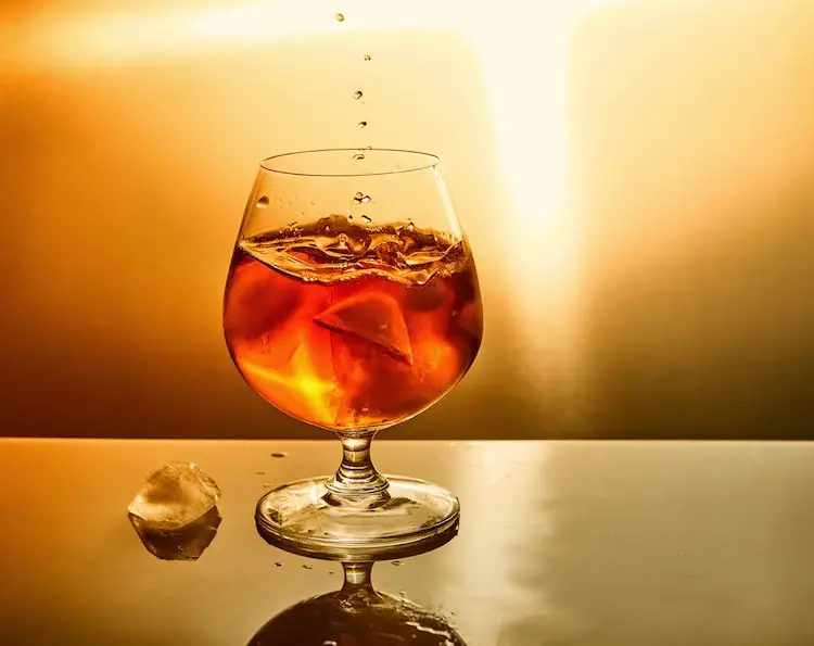 Glas whiskey mit tropfen und eis auf orangefarbenem hintergrund. glas whiskey und tropfen symboldesign.