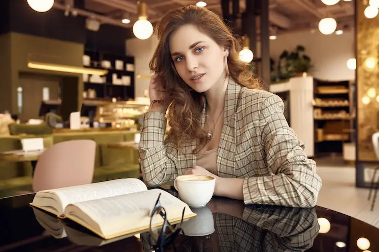 Porträt der jungen schönen frau trinkt kaffee und liest buch im caféinnenraum