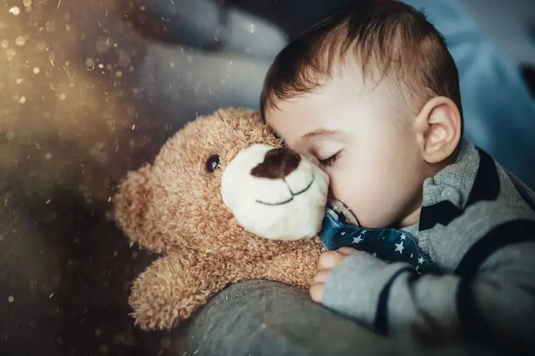 er junge schläft süß auf einem beigefarbenen teddybär auf graublauem hintergrund