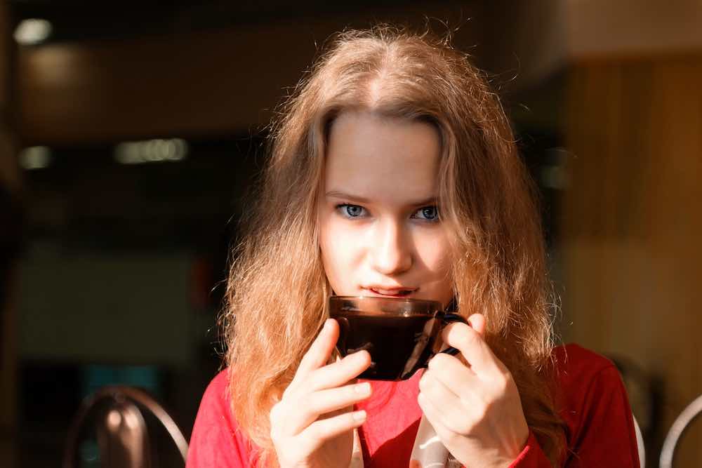 Porträt eines jungen hübschen mädchens mit einer tasse kaffee, die an einem sonnigen tag vor dem fenster sitzt. unscharfer hintergrund.