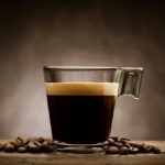Schwarzer kaffee in glastasse mit kaffeebohnen auf holztisch