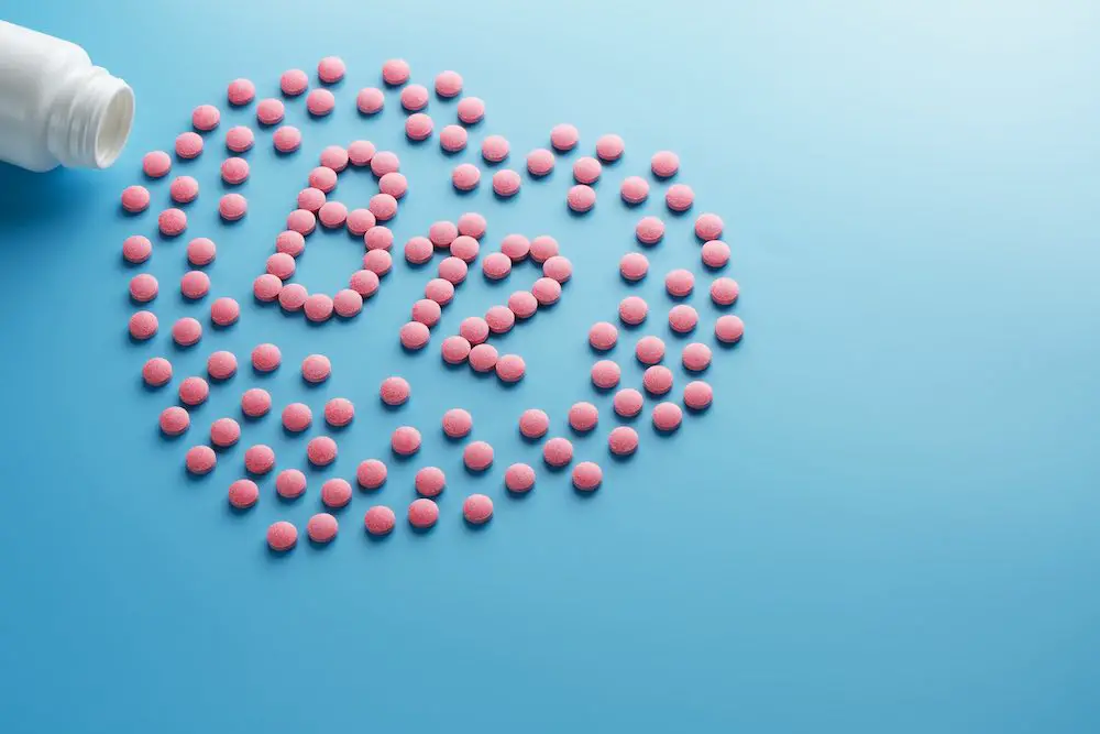 Rosafarbene tabletten in form von b12 im herzen auf blauem hintergrund, verschüttet aus einer weißen dose. nahrungsergänzungsmittel-konzept