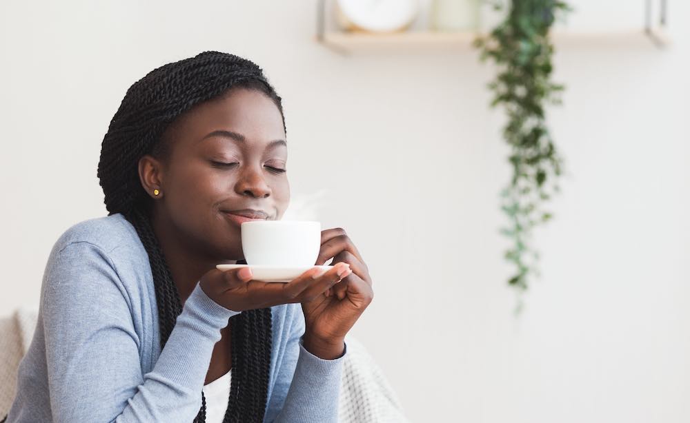 Afroamerikanisches mädchen, das eine tasse kaffee hält und seinen aromatischen geruch genießt und sich zu hause entspannt