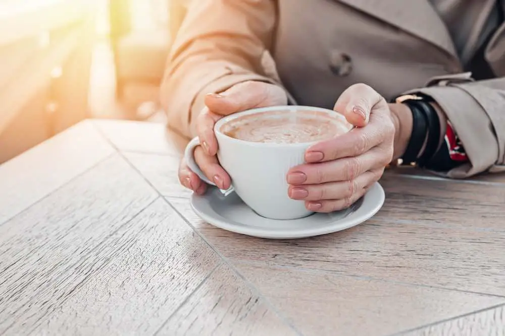 Große weiße tasse kaffee in den händen der frau mit pastellmaniküre beim sitzen im café. zugeschnitten, platz kopieren.
