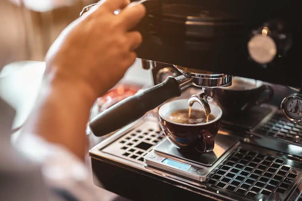 Close-up-kaffeemaschine, die professionell kaffee von barista mit einem tiefweißen glas im abendsonnenlicht extrahiert. kaffee, extraktion, tief, maschine, machen, barista-konzept.