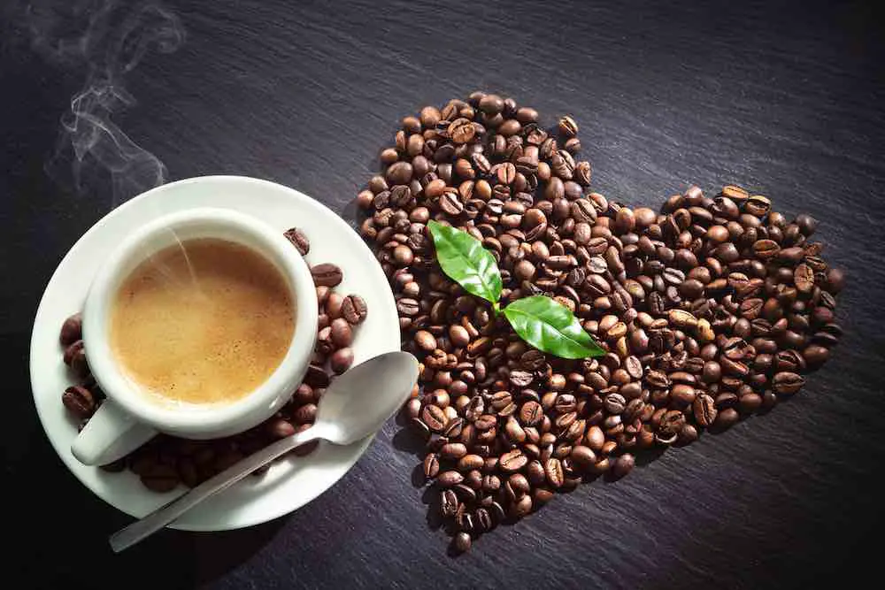 Tasse espresso und kaffeebohnen in herzform auf dunklem schieferhintergrund