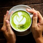 Die hand der frau hält eine tasse matcha latte auf einem alten holztisch, grüner tee auf einem alten holztisch