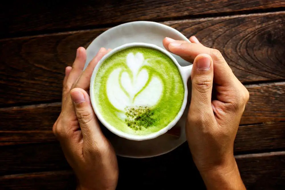 Die hand der frau hält eine tasse matcha latte auf einem alten holztisch, grüner tee auf einem alten holztisch