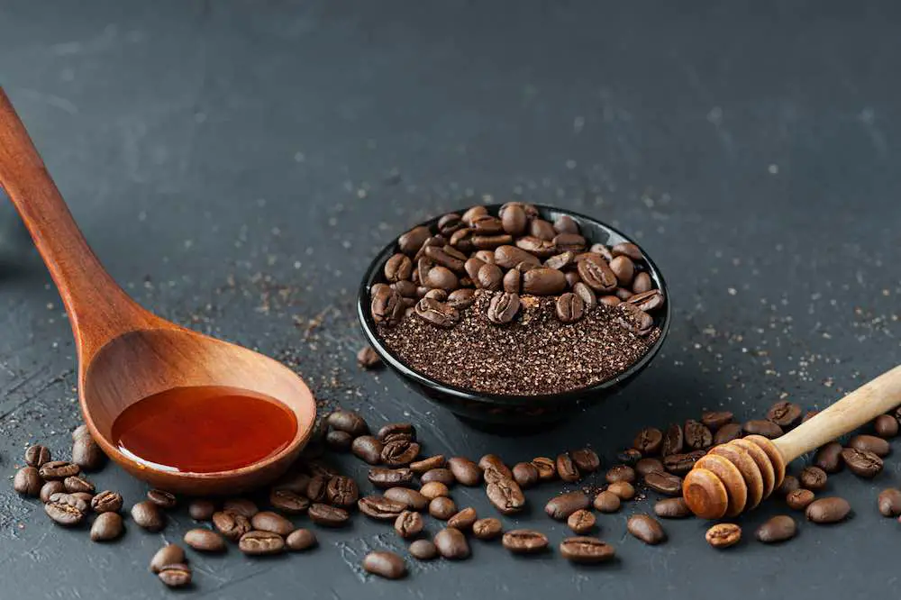 Kaffeepeeling und kaffeebohnen in schwarzem porzellanglas, honig, kosmetiköl und holzstab für honig vor dunklem zementhintergrund, körperpflege zu hause, layout von anti-cellulite-hautprodukten