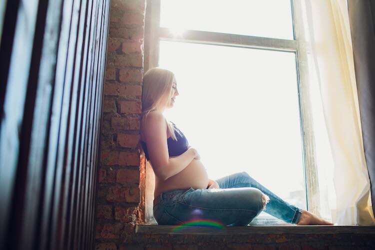 Junge schöne schwangere frau sitzt zu hause auf der fensterbank