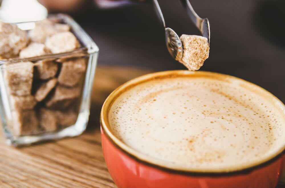 Ein stück brauner zucker wird mit cappuccino in die tasse gegeben.