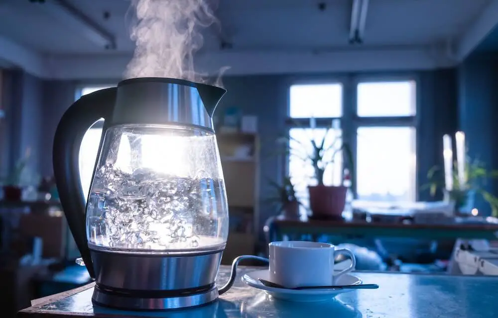 Ein transparenter wasserkessel kocht vor dem hintergrund des sonnenuntergangs, der durch das fenster scheint. das konzept der kaffeepause und des endes des arbeitstages.