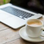 Technik, wirtschaft und das moderne leben konzept-ende des offenen laptop-computer und kaffeetasse auf dem tisch im büro oder hotelzimmer bis