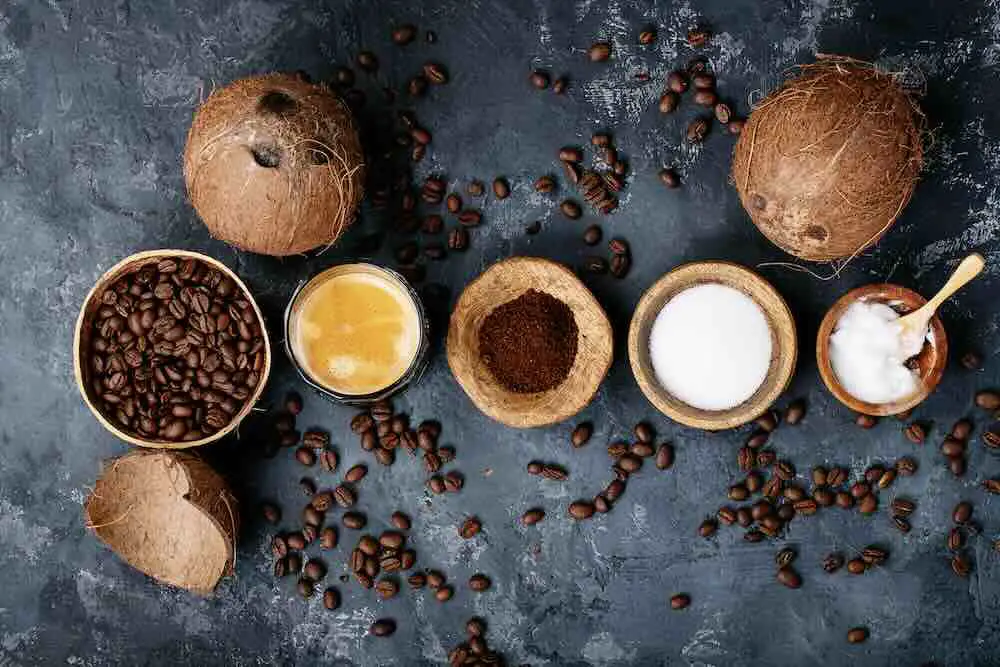 Kugelsicherer Kaffee serviert mit gemahlenen und ganzen Kaffeebohnen, Kokosnüssen, Kokosöl auf dunklem Texturhintergrund. Ansicht von oben, flach liegend. Platz kopieren